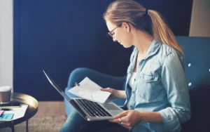 Femme consultant des documents à côté de son ordinateur portable à la maison