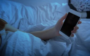 Femme allongée dans son lit utilisant son smartphone le soir