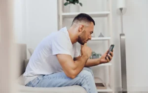 Homme pensif assis sur un canapé regardant son smartphone